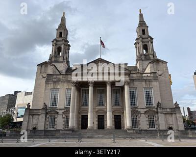 La façade néoclassique du Leeds Civic Hall à Leeds, Royaume-Uni, avec des tours jumelles, un portique en pierre et le drapeau de l'Union Jack sous un ciel nuageux. Banque D'Images