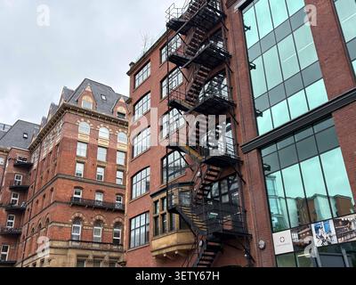 Vue en bas angle de l'architecture historique en briques rouges et une façade de bureau moderne avec une évacuation incendie en acier externe. Leeds, Royaume-Uni. Banque D'Images