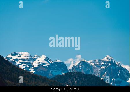 Un beau paysage minimaliste horizontal capturant les sommets ensoleillés et enneigés des Alpes Dolomites en Italie au-dessus d'une ligne de forêt de pins vert foncé Banque D'Images