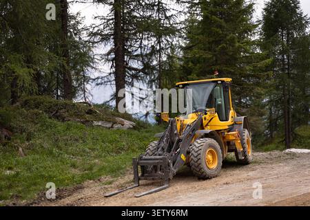 Chargeuse sur pneus compacte sur une route forestière dans les Alpes italiennes lors de travaux d'infrastructure de montagne. Banque D'Images
