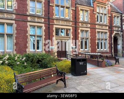 Bâtiment universitaire historique en brique rouge avec garniture en pierre à Leeds, Royaume-Uni, avec un banc de parc en bois et une poubelle générale au premier plan. Banque D'Images
