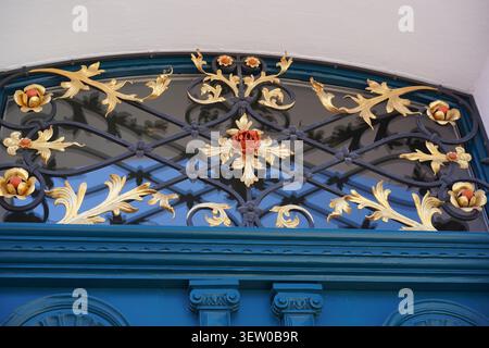 Grille de tableau arrière ornée en fer forgé avec des ornements dorés et une rose rouge sur une porte bleue historique dans la vieille ville de Stralsund, en Allemagne. Banque D'Images