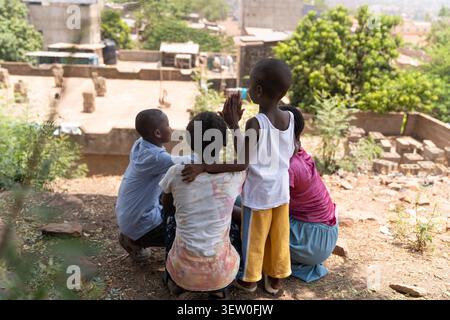 Les frères et sœurs africains s'assoient et se tiennent ensemble sous l'arbre, leurs mains levées se réunissant dans un geste ludique qui capture la proximité, la confiance et le partage h. Banque D'Images