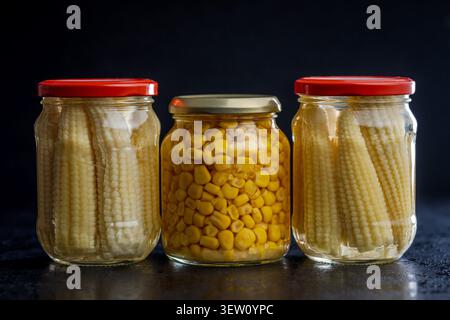 Trois bocaux en verre remplis de maïs bébé et de grains de maïs jaune vif, présentant des légumes conservés pour garde-manger, cuisine maison et stockage des aliments. Guerre Banque D'Images
