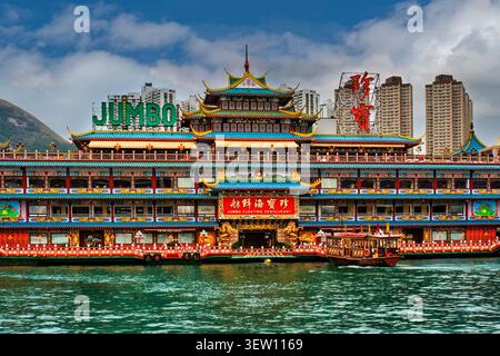 L'ancien restaurant flottant Jumbo dans le port d'Aberdeen, Hong Kong, avec un bateau portuaire traditionnel passant au premier plan. Banque D'Images