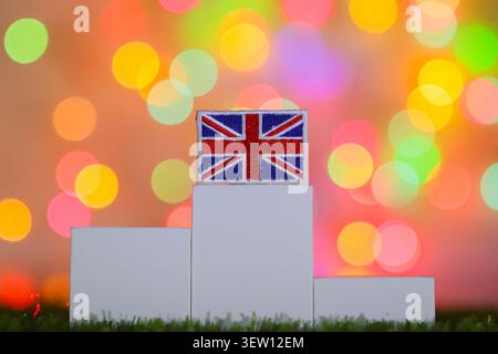 Le drapeau de l'Union du Royaume-Uni est affiché sur le plus haut niveau d'un podium blanc vainqueur à trois niveaux sur un fond abstrait coloré bokeh clair. Banque D'Images