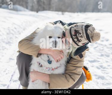 Portrait d'une femme caucasienne serrant son chien Samoyed lors d'une promenade hivernale. Banque D'Images