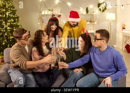 Amis grillant du champagne à la maison pendant la fête de Noël, riant ensemble Banque D'Images