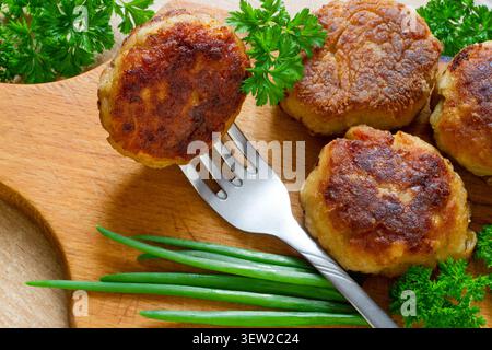 Escalope de viande sur une fourchette. Côtelettes avec des herbes sur une planche à découper. Galettes de viande avec oignons verts et persil. Banque D'Images