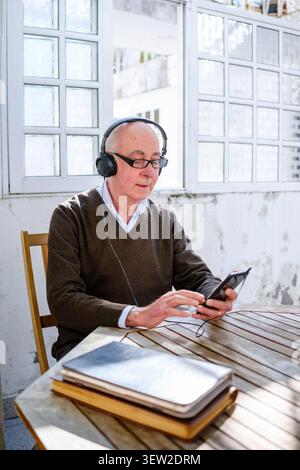 Homme senior appréciant la musique et le contenu numérique sur smartphone avec casque Banque D'Images
