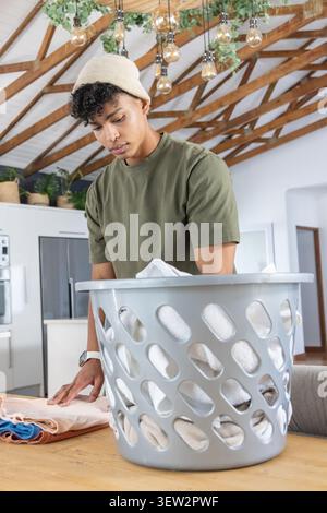 Homme pliant le linge sur la table en bois dans la cuisine de la ferme avec panier à linge en plastique gris Banque D'Images