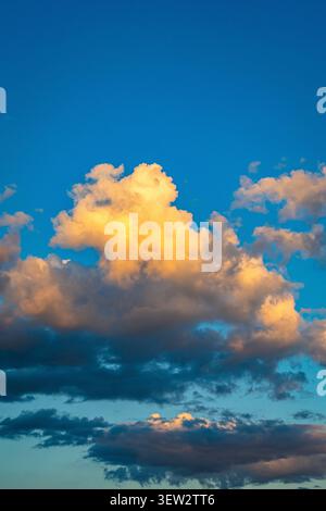 Les cumulus ensoleillés s'élèvent contre un ciel bleu profond avec des bords chauds de soirée et des mèches dispersées capturant le drame du temps changeant et la beauté de golde Banque D'Images
