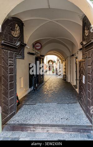 Vue à travers une entrée en arc avec de grandes portes en bois cloutées dans une cour pavée du centre historique de Prague, République tchèque. Banque D'Images