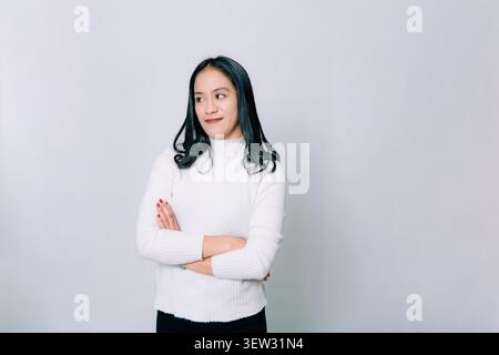 Femme asiatique pensive avec les bras croisés regardant loin sur fond blanc Banque D'Images
