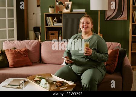 Portrait de femme grande taille se relaxant avec Smoothie pendant Home Break Banque D'Images