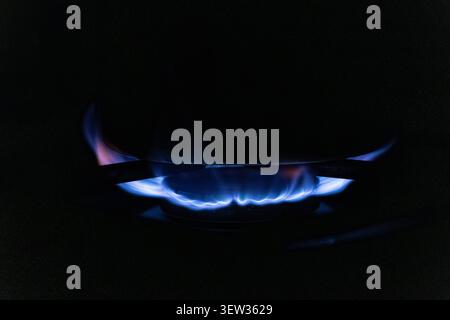 Feu bleu vif brûle régulièrement sur un brûleur de cuisinière de cuisine moderne sous une casserole, illustrant le processus de préparation des aliments à la maison avec un accent sur cl Banque D'Images