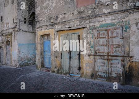 Une ruelle étroite présente trois vieilles portes altérées dans un bâtiment en pierre en ruine avec de la peinture écaillée. Les portes sont peintes dans différentes nuances Banque D'Images