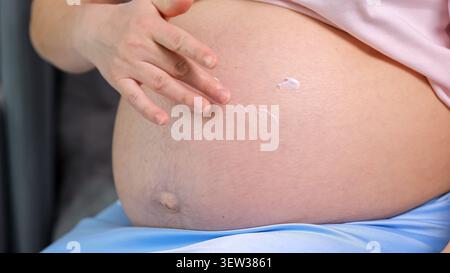 Femme enceinte appliquant une lotion hydratante sur son ventre Banque D'Images