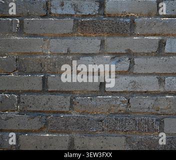 Mur de briques récupérées peint en noir avec des briques lisses et rugueuses, peinture écaillée révélant la brique et le mortier sous-jacents Banque D'Images