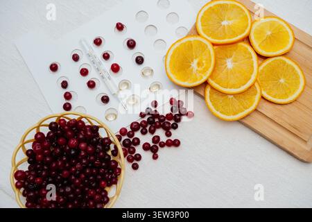 Une composition à plat présentant des moyens naturels de soutenir l'immunité, avec un bol de canneberges fraîches, des tranches d'orange sur une planche de bois, Banque D'Images
