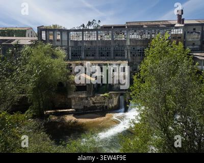 Façade grungy d'une usine de textile abandonnée assise sur les rives de la rivière Nabao dans le centre du Portugal Banque D'Images
