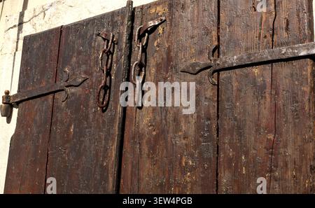 Un gros plan de volets de fenêtres sombres et anciens en bois présentant des textures fortement altérées, de longues charnières en fer rustique et des chaînes de sécurité suspendues. Banque D'Images