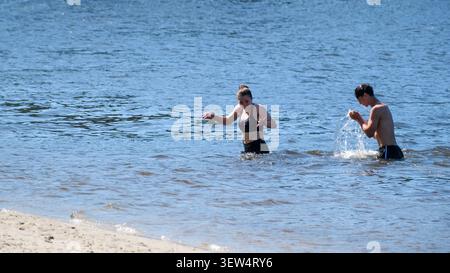 Deux amis éclaboussent de l'eau tout en profitant du soleil chaud à la plage. Kiev, Ukraine, 25 juin 2026 Banque D'Images