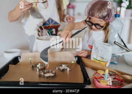 Maman et enfant préparant des biscuits ensemble à la maison en utilisant des emporte-pièces dans une cuisine lumineuse Banque D'Images