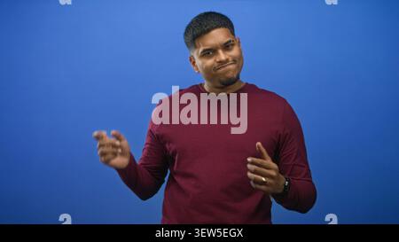 Homme haussa les mains avec une expression méprisante dans un studio bleu portant un pull marron et une montre-bracelet, paumes visibles et les yeux fermés ; amusement doux. Banque D'Images