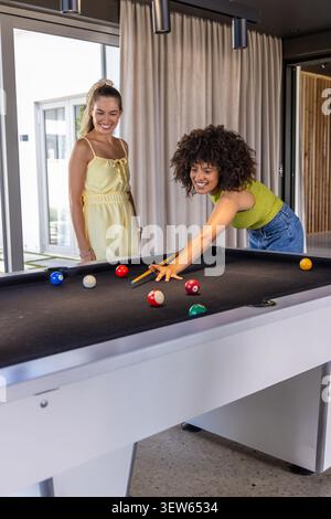 Amies féminines diverses jouant au billard dans la salle de Rec, se penchant sur une table en feutre noir à l'aide d'un bâton de queue Banque D'Images