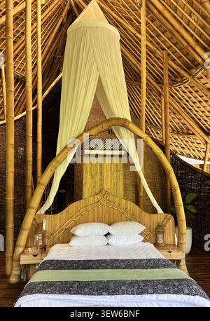 Chambre avec un lit à baldaquin en bambou drapé de moustiquaire blanche à l'intérieur d'une villa de luxe en bambou écologique, Ubud, Bali, Indonésie. Banque D'Images