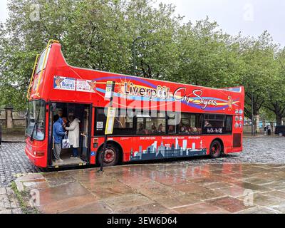 Un bus touristique rouge vif à deux étages à Liverpool, au Royaume-Uni, avec des passagers embarquant à un arrêt de rue un jour de pluie. Banque D'Images