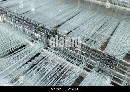Vue rapprochée du processus de tissage dans une usine de production de laine, présentant les machines complexes et les fils utilisés dans la filature et le tissage. Banque D'Images