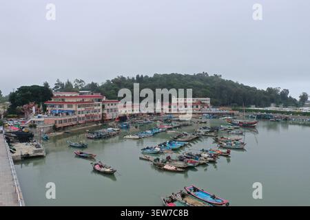 Une vue de drone à angle élevé surplombe un port de pêche animé où des dizaines de bateaux en bois colorés sont densément amarrés dans une crique abritée, avec une petite mer Banque D'Images