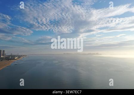 Une vue par drone montre une rangée de gratte-ciels modernes et de tours de grande hauteur s'élevant d'un banc de brouillard côtier à Xiamen, avec des collines verdoyantes et un rivage incurvé Banque D'Images