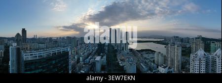 Un grand drone panoramique capture une ville côtière tentaculaire à l'aube, avec des rayons de soleil qui traversent un grand nuage au-dessus des tours jumelles et Banque D'Images