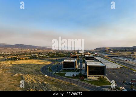 Vue aérienne des immeubles de bureaux modernes et des parkings avec une autoroute longeant le paysage urbain sous un ciel brumeux au-dessus du lointain mountai Banque D'Images