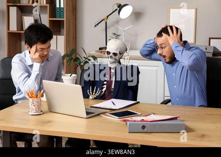 Collègues masculins stressés avec squelette humain à table au bureau Banque D'Images