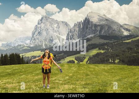 Vue arrière moyen âge cheveux gris femme randonneur bras étendus avec sac à dos jaune surplombant la vallée alpine verte luxuriante montagnes brumeuses fond Dol Banque D'Images