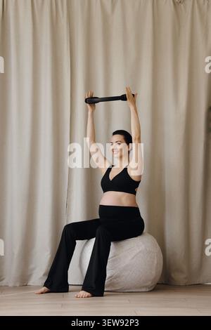 Femme enceinte assise sur le ballon de fitness tenant l'anneau de pilates pendant l'entraînement prénatal Banque D'Images