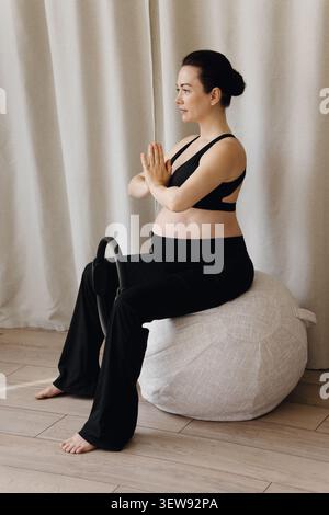 Femme enceinte assise sur le ballon de fitness tenant l'anneau de pilates pendant l'entraînement prénatal Banque D'Images