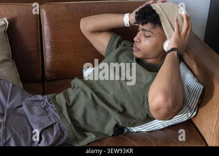 Homme afro-américain au début des années 20 s'inclinant sur un canapé à la maison portant des écouteurs ajustables bonnet Banque D'Images