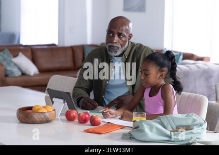 Homme aîné afro-américain et jeune fille étudiant ensemble au comptoir de cuisine blanc à l'aide d'une tablette Banque D'Images