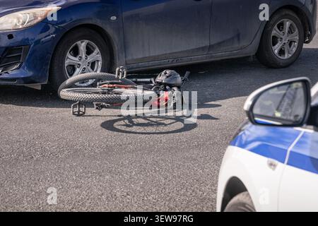 Bicyclette endommagée couchée sur la route après une collision avec une voiture alors qu'une voiture de police se présente sur les lieux de l'accident. Image éditoriale montrant un accide cycliste Banque D'Images