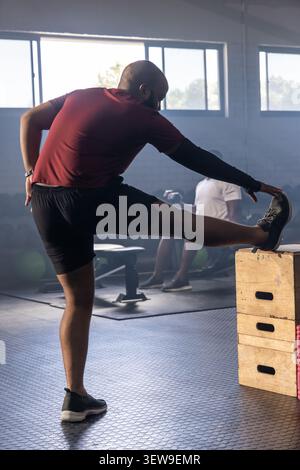 Divers hommes de gymnastique étirant la jambe droite sur des boîtes en bois empilées en plyo à la salle de gym, regardez visible Banque D'Images