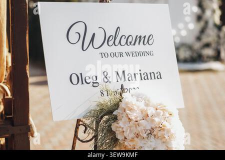 Signe de bienvenue pour une célébration de mariage. Arrangement floral doux sous l'écriture élégante. La date du mariage est subtilement affichée sous les noms. Les tons chauds sucrent Banque D'Images