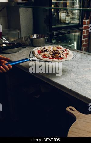 Une pizzeria place une pizza pour une cuisson ultérieure dans le four Banque D'Images