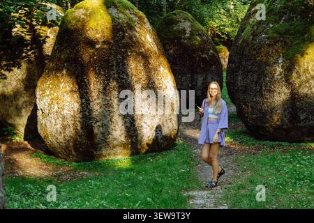 Femme debout parmi de grands rochers couverts de mousse sur le chemin forestier à Europos Parkas, Parc de l'Europe, près de Vilnius, Lituanie Banque D'Images