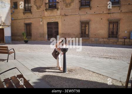 Femme buvant dans une fontaine d'eau publique sur une place de la ville Banque D'Images