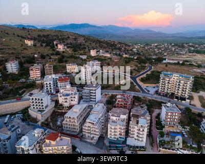 Vue aérienne des immeubles d'appartements modernes et des hôtels nichés sur la colline surplombant le paysage côtier au coucher du soleil à Sarande, comté de Vlore, Alb Banque D'Images
